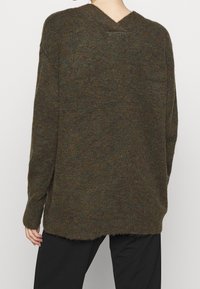 Överdimensionerad stickad tröja i mörkbrun med gröna och blåa inslag. V-ringad design med råa kanter och sänkt axel, med ribbade ärmslut.