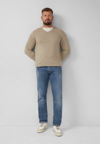 Beige V-Ausschnitt-Pullover, hellblaue Jeans und weiße Sneaker. Der Pullover ist aus weichem Strick; die Jeans sind im Straight-Leg-Schnitt mit einem verblassten Look.