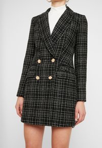 Black and white checked blazer dress with double-breasted front, gold-tone buttons, tailored fit, and textured fabric.