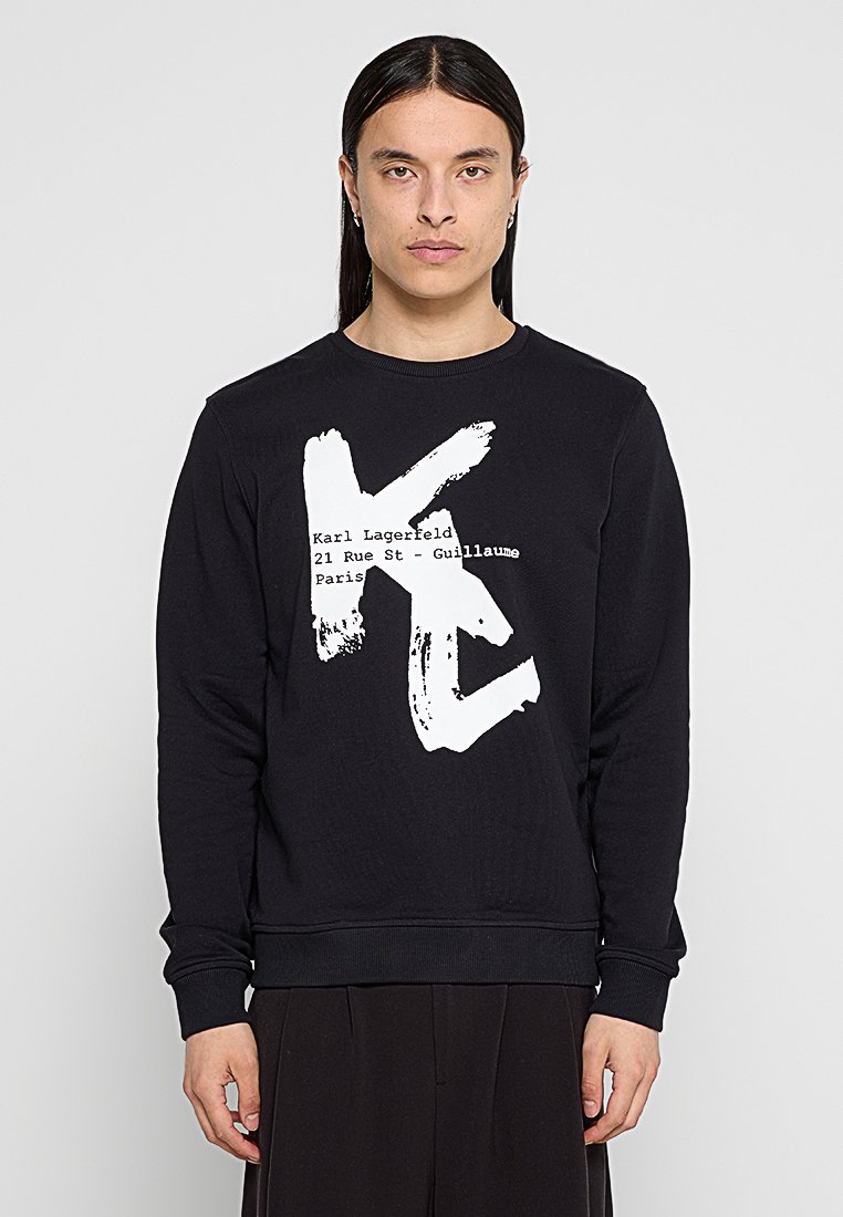 Sudadera negra con un audaz gráfico en blanco que dice "Karl Lagerfeld 21 Rue St - Guillaume París." Cuello redondo y puños acanalados.