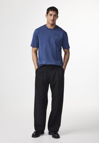 Blå bomullströja med korta ärmar och rundad halsringning, kombinerad med svarta plisserade byxor. Outfiten har en minimalistisk design och struktur.