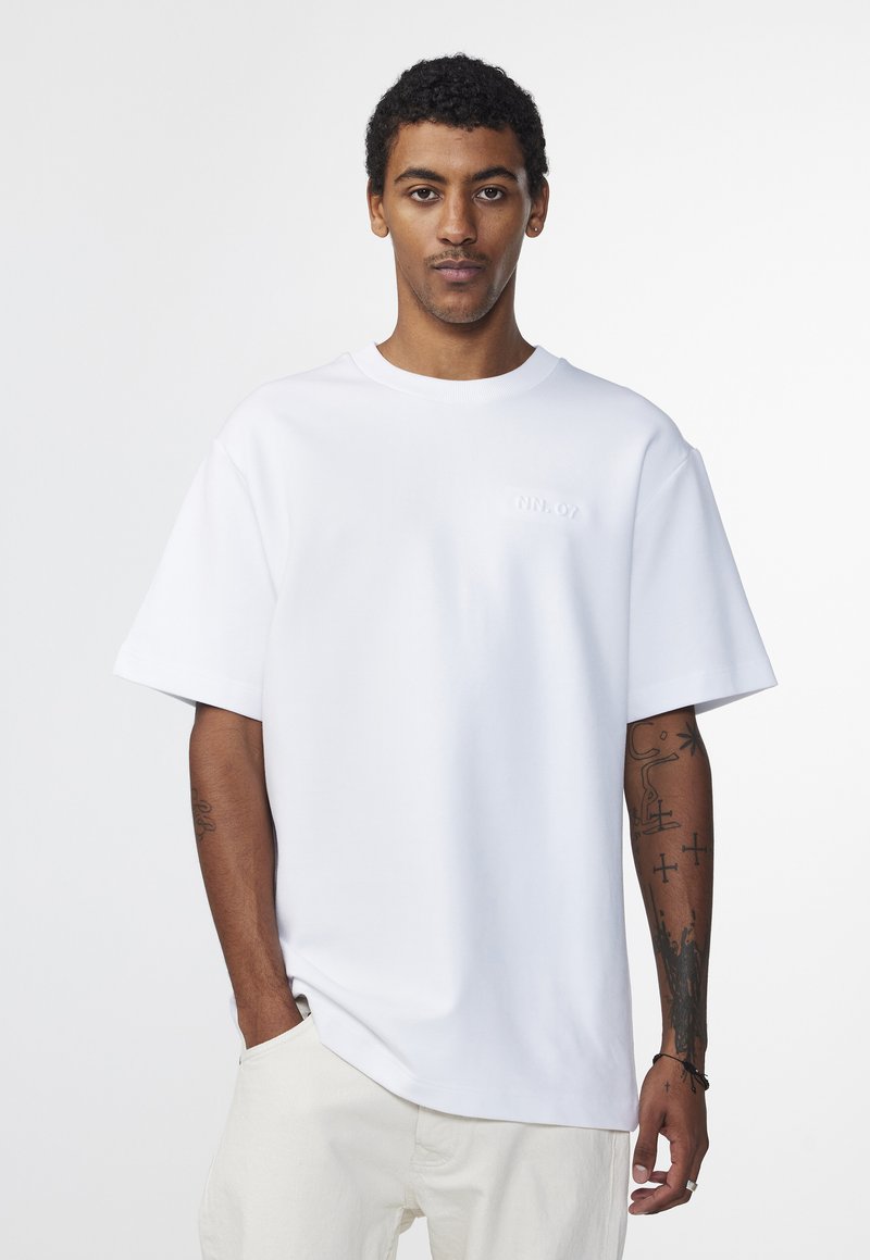 Weißes T-Shirt mit kurzen Ärmeln, lockerem Schnitt und geripptem Rundhalsausschnitt. Mit dezentem Branding in erhabenen Buchstaben auf der Brust.