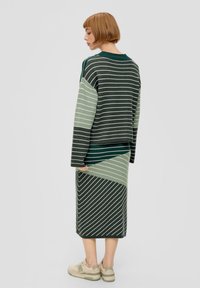 Breikleding met groen en grijze horizontale en diagonale strepen. Bevat een boxy sweater en een rok tot de knie, gecombineerd met beige sneakers.