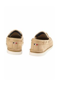 Tan suède loafers met witte rubberen zolen, lederen veters en een kleine stoffen accentvlag op de hiel. Rond ontwerp met stikdetails.