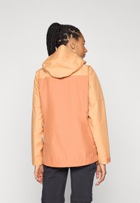 Vattentålig jacka i nyanser av orange och persika; har huva och en strömlinjeformad design; tillverkad av smidigt, lättviktigt tyg.