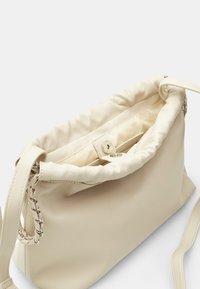 Crèmekleurige leren handtas met een geplooide bovenkant, zilveren kettingaccent en een binnenvak. Heeft een zachte, gladde textuur en een afneembare band.