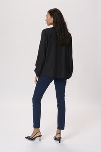 Black blouse with textured fabric, long sleeves, and relaxed fit, paired with dark blue slim jeans and black slingback heels.