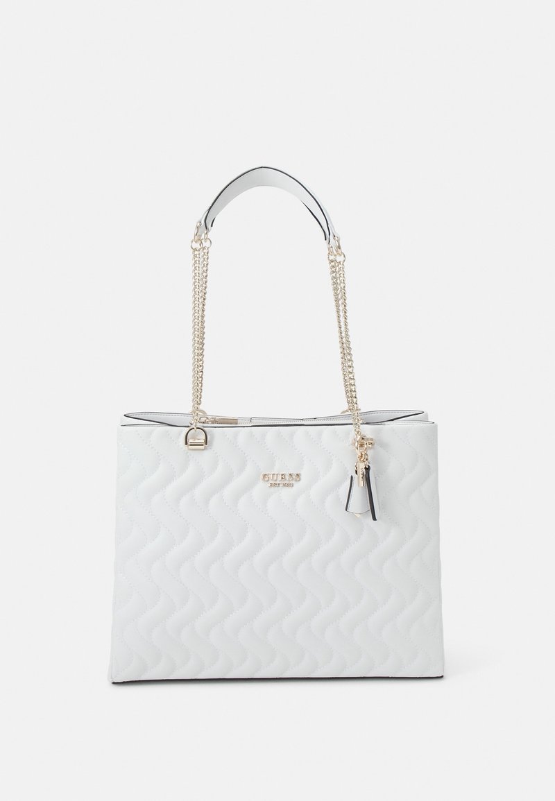 Bílá prošívaná taška přes rameno s rukojetí z stříbrného řetízku, s vyraženým logem na přední straně a přívěskem jako detailem. Má pevný tvar a hladký povrch.