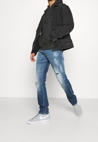 Musta denimtakki harmaan hupparin päällä, yhdistetty vaaleansinisiin kuluneisiin farkkuihin ja harmaisiin Nike-tennareihin. Rentoa asua, jossa kerroksittain erilaisia tekstuureja.