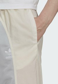 Gaismas, krēmkrāsas šorti ar pelēku sānu paneļa. Iekļauj izšūtu baltu Adidas logo un sānu kabatu.