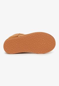 Suela de zapato de goma marrón con patrón texturizado y letras en relieve. Forma ligeramente curvada con un borde liso.