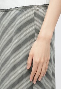 Gråstribet nederdel med letvægtsstof og diskret glans. Taljebåndet er rynket med en fin sort kant langs kanten.