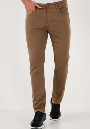 Brown stretch denim trousers with a slim fit, featuring front pockets, back pockets, and a classic button closure. Worn with black sneakers.