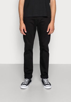 Schwarze Denim-Hosen mit schmaler Passform, ausgestattet mit klassischem Fünf-Taschen-Design, umgeschlagenen Säumen, kombiniert mit schwarz-weißen Low-Top-Sneakern.