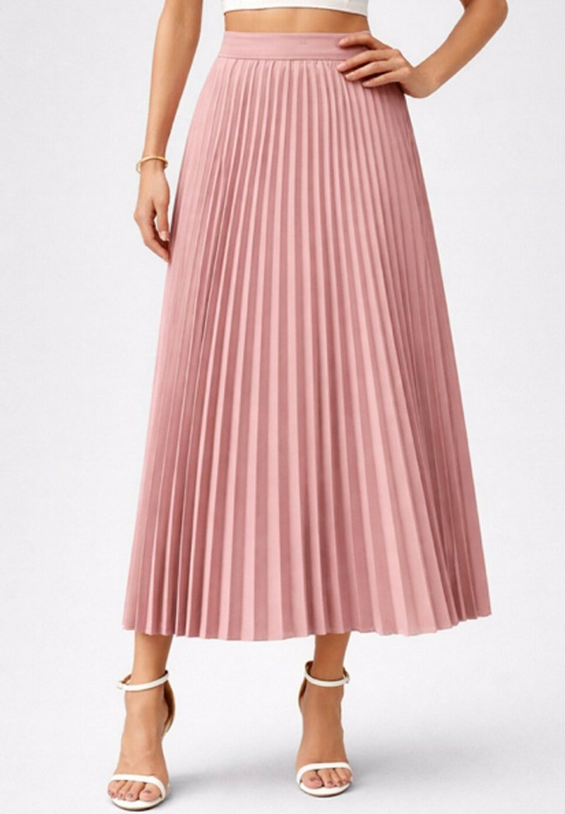 Femme portant une jupe midi plissée taille haute rose poudré avec des talons blancs à bride cheville, debout avec une main sur la hanche.