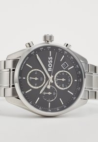 Χρονογράφος ρολόι από ανοξείδωτο ατσάλι με μαύρο καντράν, silber  ενδείξεις και τρεις υποκαντράν. Διαθέτει παράθυρο ημερομηνίας και κλίμακα ταχυμέτρου.