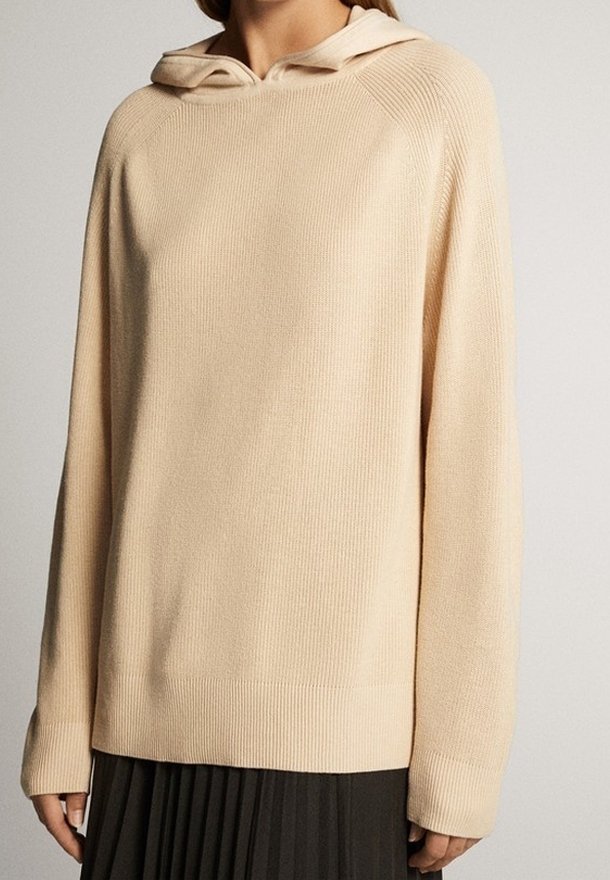 Sweat à capuche de couleur crème avec une texture côtelée, doté d'une capuche avec cordon de serrage, de manches longues et d'une coupe décontractée. Design simple et minimaliste.