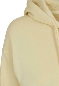 Sweat à capuche beige montrant l'épaule, le haut de la manche et la capuche avec un détail cordon sur un fond uni.