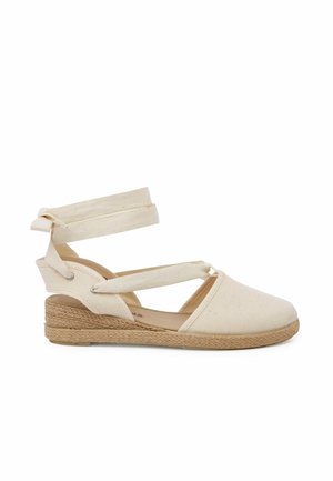 Beige canvas espadrille schoen met een enkelbandje, met een geweven jute zool. Het ontwerp heeft een gesloten teen en een open hiel.