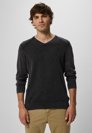 Maglione grigio scuro a v in texture a coste. Maniche lunghe con polsini aderenti. Materiale morbido; presentato su una persona contro uno sfondo neutro.