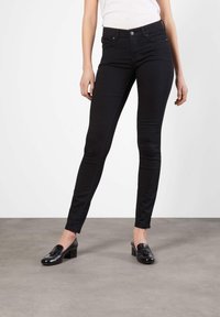 Svarte skinny jeans med mid-rise liv, laget av elastisk denim. Har knappelåsing og fem lommer, kombinert med svarte loafers.