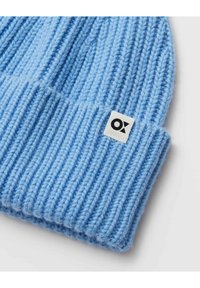 Bonnet tricoté bleu clair avec texture côtelée et revers plié. Présente une petite étiquette carrée avec le logo "OX" noir sur le côté.