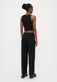 Črni izrezani top brez rokavov in široke črne hlače z rebrastim vzorcem. Hlače imajo visok pas. Model nosi masivne črne čevlje. Enostavno ozadje.