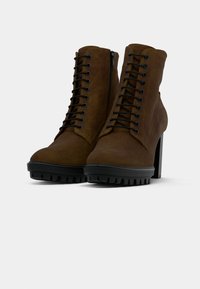 Smeškanje smeđe faux suede čizme do gležnja s visokim potpeticama, vezivanjem sprijeda i bočnim patent zatvaračem, s robusnim crnim potplatom s utorima.