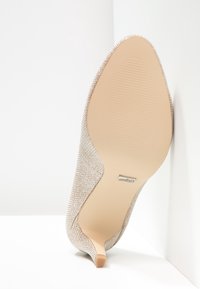 Béžová lodička na vysokém podpatku s texturovaným, tkaným svrškem, špičatou špičkou a úzkým stiletto podpatkem. Hladká, světlá podrážka s vroubkovaným detailem.
