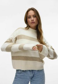 Pull rayé aux nuances crème et beige, avec un col et des poignets côtelés, coupe ample et texture douce. Associé à un jean bleu clair.