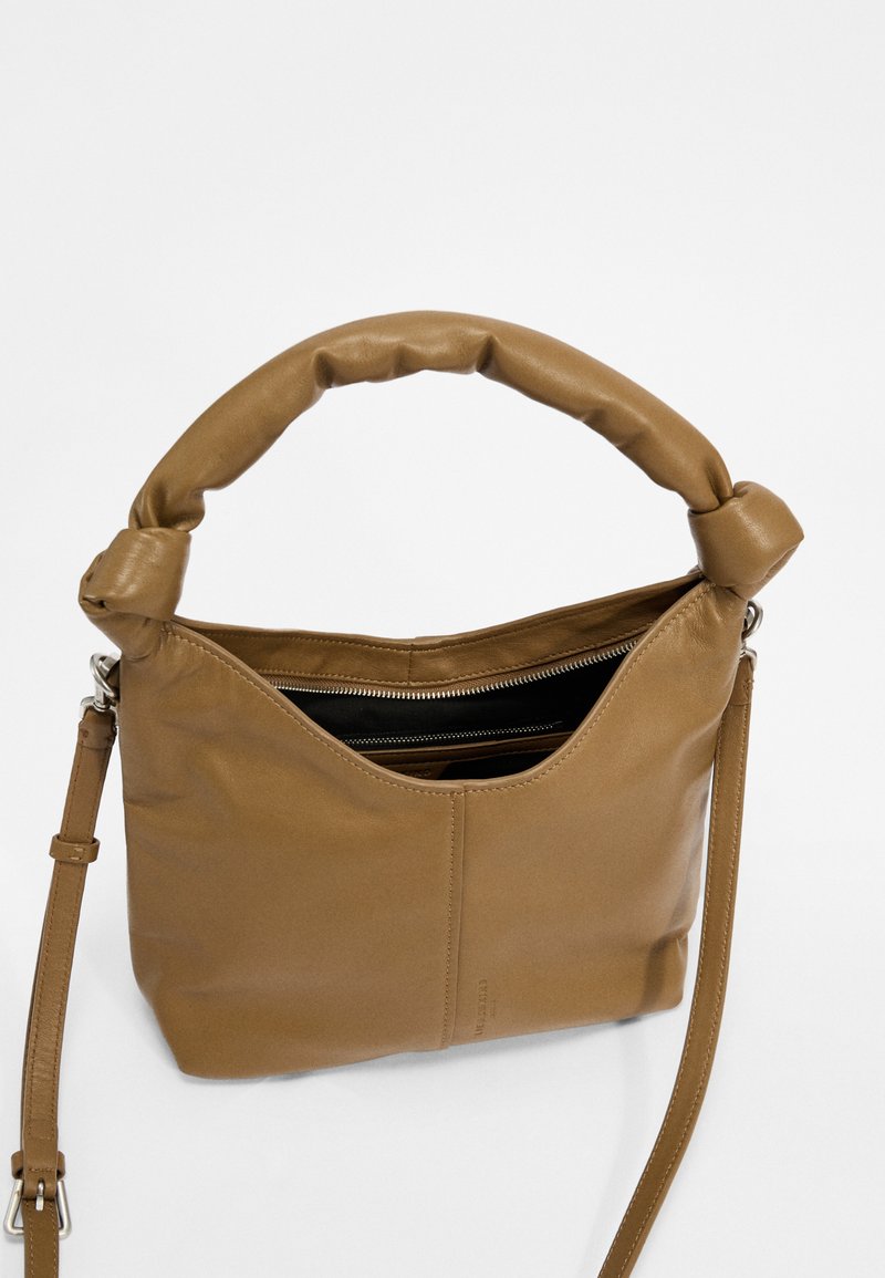 Braune Ledertasche mit einem weichen, geknoteten Griff, einem verstellbaren Trageriemen und einem Reißverschluss-Innenfach. Glatte Textur, schlichtes Design.