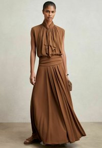 Ruskea hihaton mekko, jossa on röyhelökaulus, istuva vyötärö ja valuva poimutus. Sujuva kangas, jossa on pehmeä kiilto. Täydentää kudottu clutch-laukku.