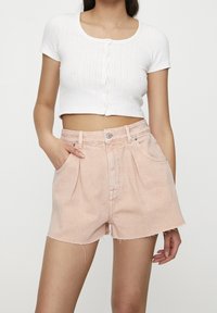 Top corto blanco con texturizado acanalado que presenta un escote redondo y cierre de botones, combinado con pantalones cortos de mezclilla de tiro alto en rosa claro con dobladillo deshilachado y bolsillos.