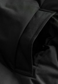Materialul negru, cu o textură netedă, dispune de un buzunar cu fermoar ascuns. Marginile sunt cusute cu atenție, având un design minimalist.