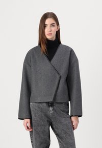 Sivi wrap kaput sa teksturiranim finišem, oversize kroja i širokim rukavima. Sadrži kontrastni crni obrub duž ivica.