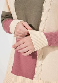 Sweter robiony na drutach z kolorowym blokiem w odcieniach kremowym, oliwkowym i mauve, z ściągaczami na rękawach oraz teksturowanym wzorem w warkocze po bokach.