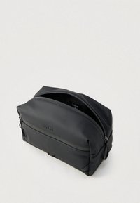 Melna neilona tualetes soma ar gludu tekstūru, apaļu dizainu, augšējo rāvējslēdzēja aizdari un reljefa logotipa detalizējumu priekšpusē.