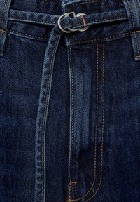Jeans in denim blu scuro con una vita aderente, caratterizzati da una cintura intrecciata che passa attraverso un anello d'argento e cuciture decorative.