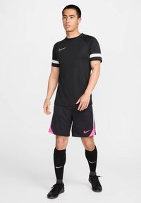Maglietta sportiva nera con accenti bianchi, pantaloni corti neri con lati rosa e calze nere lunghe fino al ginocchio. Logo Nike sulla maglietta e sui pantaloni corti.