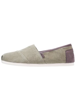 Casual slip-on sko i lysegrønt lærred med hvid sål og mørkegråt hælpatch, med et lille TOMS stofmærke på siden.