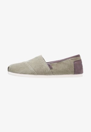 Chaussure décontractée à enfiler en toile vert clair avec une semelle blanche et un patch de talon gris foncé, avec une petite étiquette en tissu TOMS sur le côté.