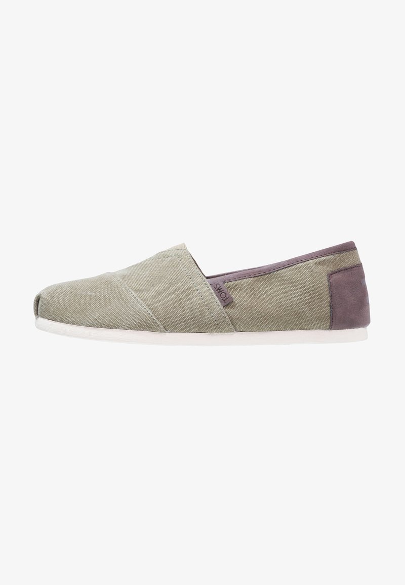 Chaussure décontractée à enfiler en toile vert clair avec une semelle blanche et un patch de talon gris foncé, avec une petite étiquette en tissu TOMS sur le côté.
