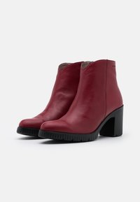 Rote Lederstiefeletten mit spitzer Zehenform und Gummiblattform, die eine glatte Textur und eine subtile gebogene Öffnung oben aufweisen.