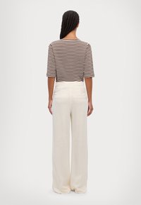 Gestreept bruin-wit topje met korte mouwen, gecombineerd met hooggetailleerde beige broek met wijde pijpen en achterzakken.