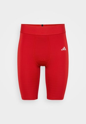 Red athletic shorts made from stretchy material, featuring a fitted design, elastic waistband, and a small white logo on the lower side.