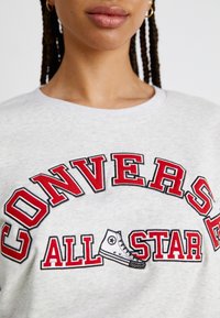 Sudadera gris con texto bordado en rojo y negro que dice "CONVERSE ALL STAR", acompañado de una ilustración de una zapatilla de caña alta.