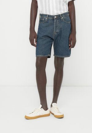 Shorts en denim bleu à coupe droite, avec cinq poches et des accents de couture. Associés à des baskets blanches et une chemise à manches courtes à rayures claires.