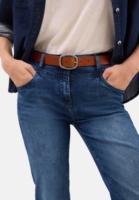 Blaue Denim-Jeans mit einer taillierten Passform, ausgestattet mit einem braunen Leder-Gürtel mit einer silbernen Metallschnalle. Taschen sind auf beiden Seiten sichtbar.