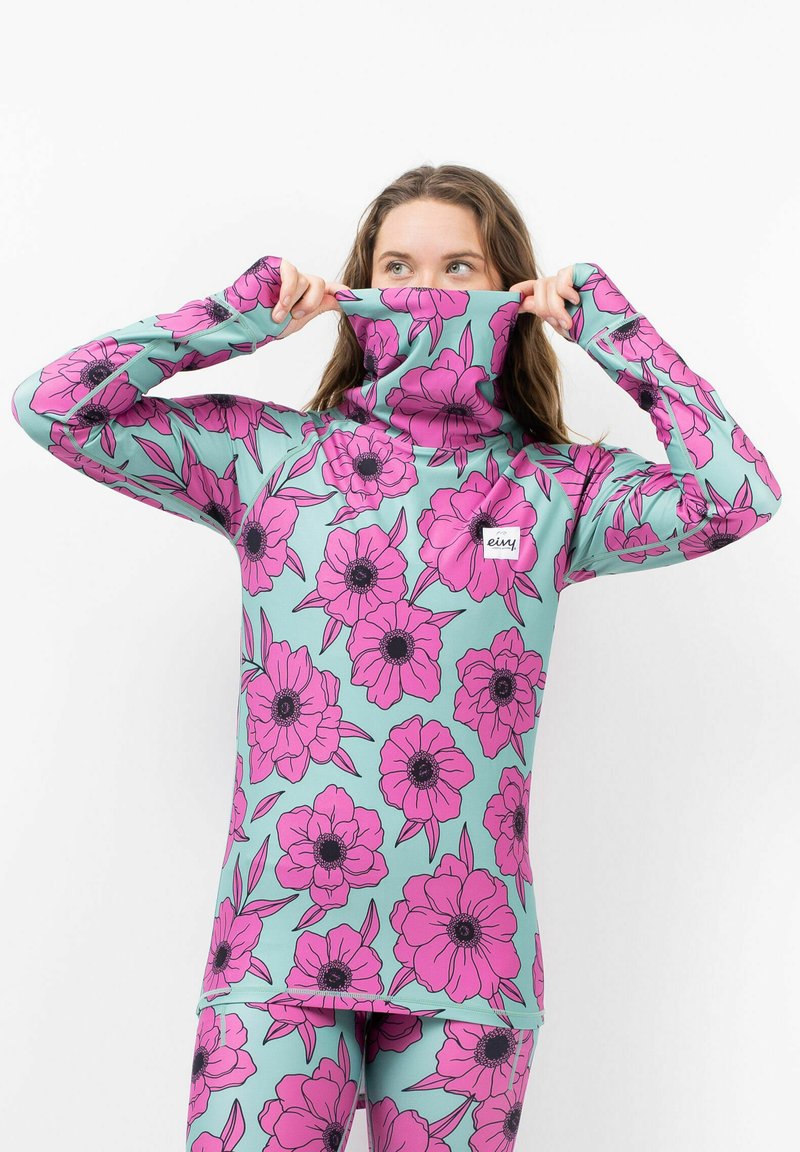 T-shirt à manches longues en vert menthe avec de grands motifs floraux roses. Doté d'un col haut et pliable et d'une coupe ajustée. Étiquette de la marque visible sur la poitrine.