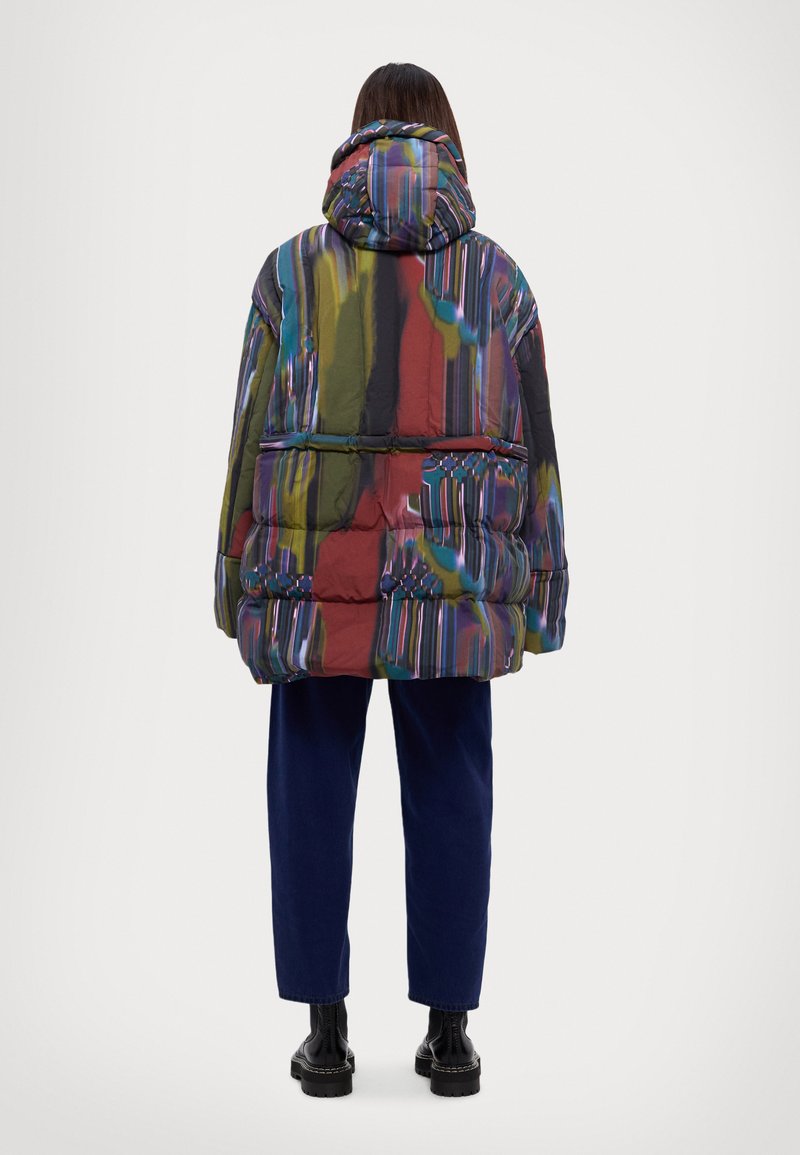 Veste rembourrée avec un motif abstrait multicolore, dotée d'une capuche, de poches avant et d'une coupe décontractée. Portée avec un pantalon bleu marine et des bottes noires.